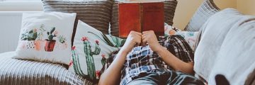 A man laying on the sofa reading a book