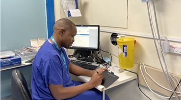 Clinical worker sitting at desk in hospital with ipad