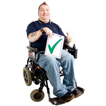 Person in an electric wheelchair holding a sign with a green tick