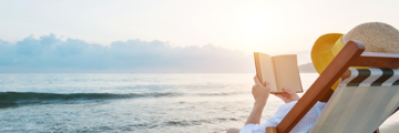 Image of a person on the beach, sitting in a chair reading a book.