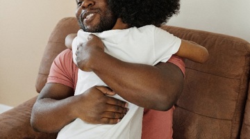 A man in a red t-shirt hugging a boy in a white t-shirt